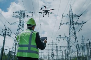 technician controlling drone near high voltage power lines, focusing on inspection screen, electrical towers